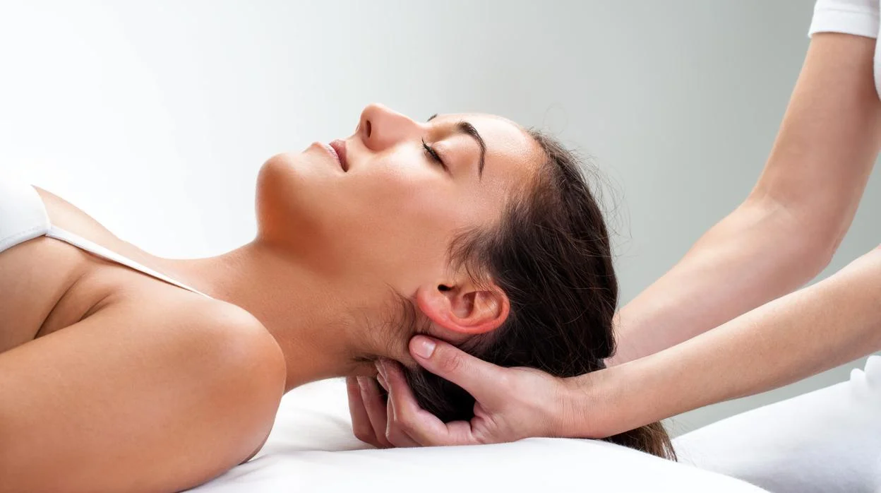 Mujer recibiendo un masaje en el cuello y la cabeza en un entorno relajante, con una mano aplicando presión suavemente. Ideal para reducir el estrés y mejorar la circulación.